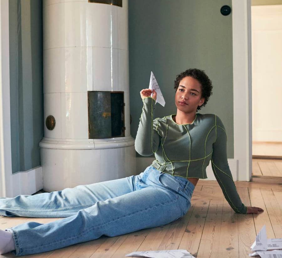 Person sitting on the floor holding a folded piece of paper, surrounded by scattered documents in a calm home environment