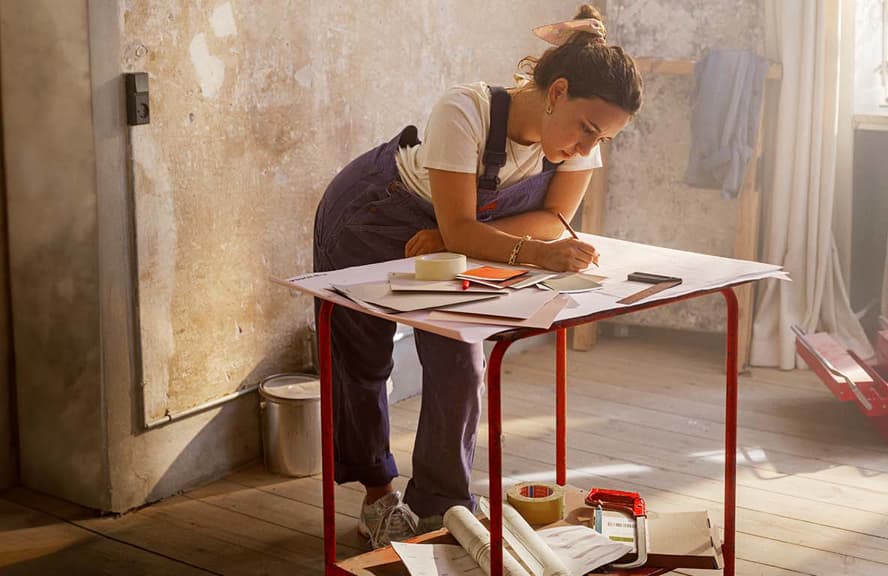 Person planning a home renovation project at a table in a sunlit room with unfinished walls