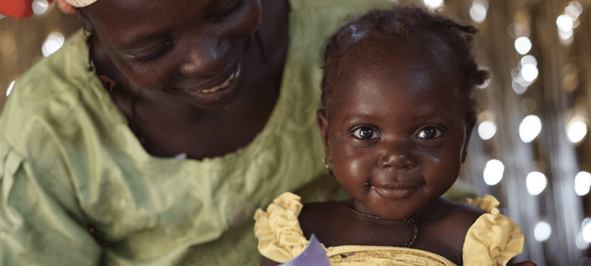 Smiling baby in a yellow dress being held by an adult in a green top