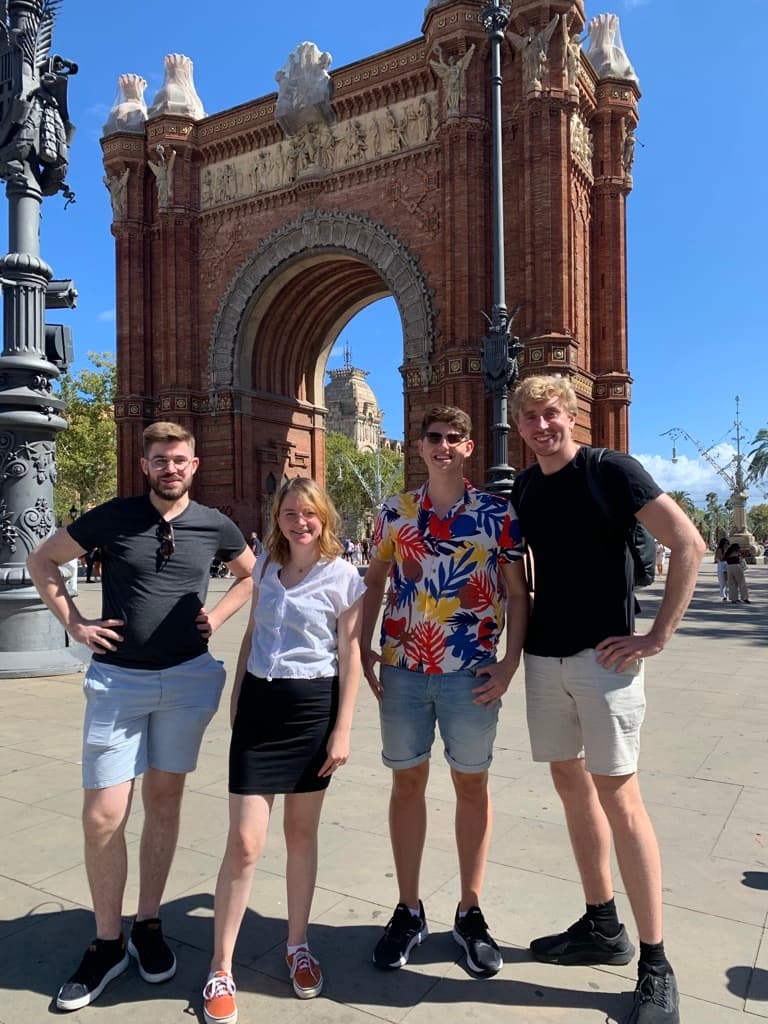Four people standing and smiling in front of the Arc de Triomf in Barcelona on a sunny day