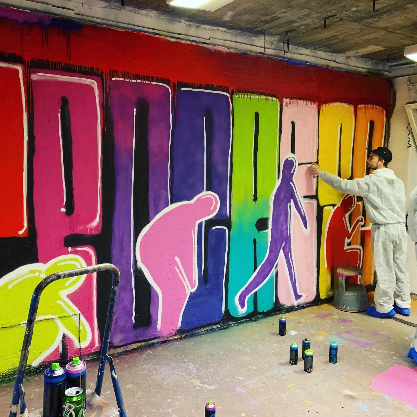 A colleague painting colorful silhouettes on a wall during Swace’s office graffiti workshop.