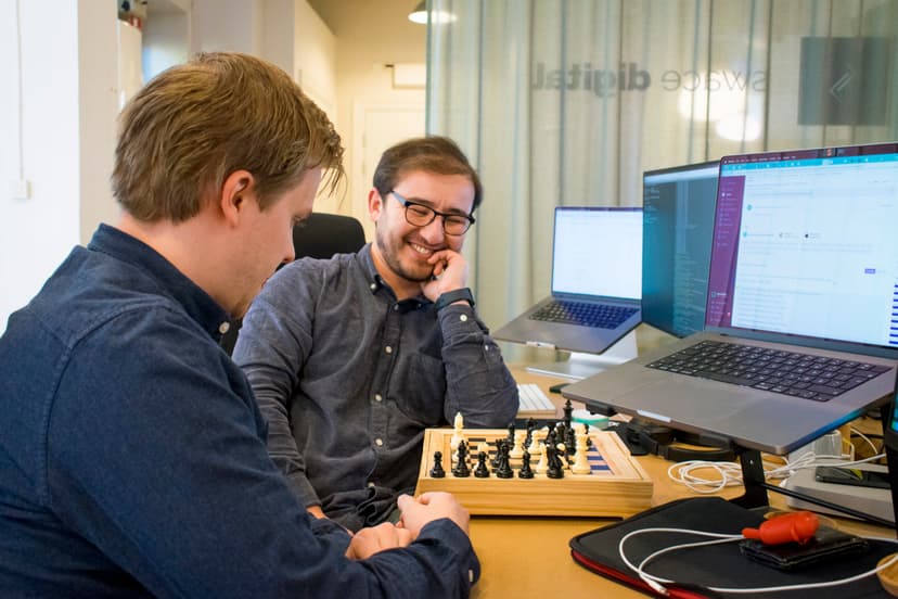 Two colleagues sitting at a desk in the Swace office, smiling while playing chess during a break.