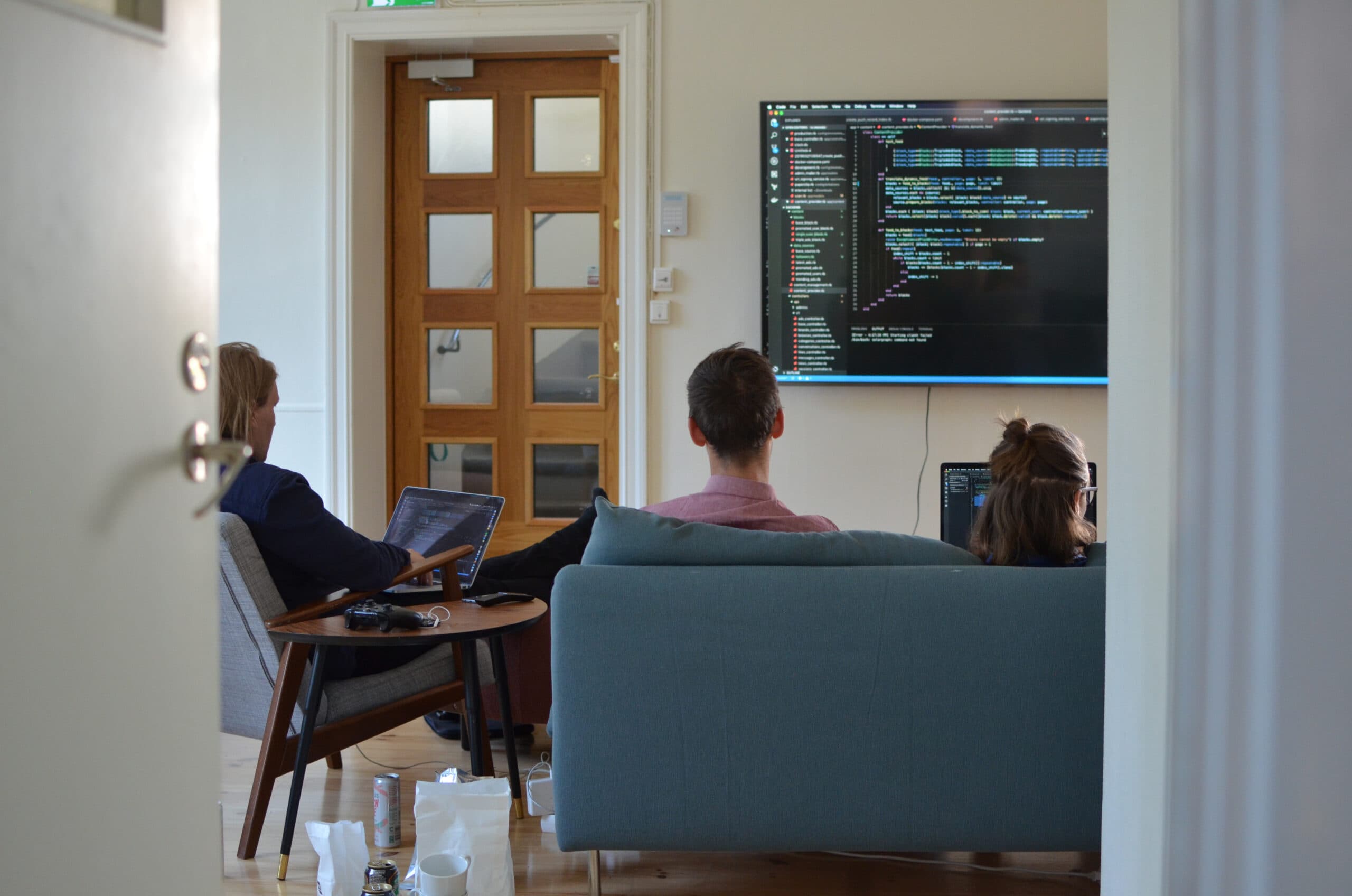 Three colleagues sitting in the office, collaborating on code displayed on a large screen.