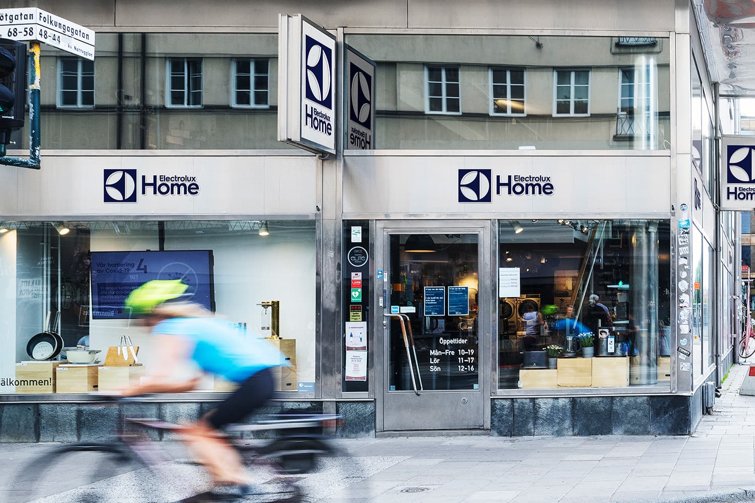 Street view of an Electrolux Home storefront on Götgatan in Stockholm. A cyclist rides past the entrance, with product displays and signage visible through the windows.