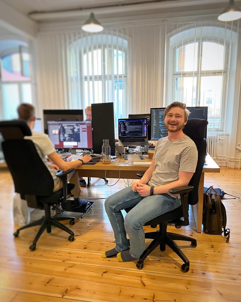 Two colleagues working at their desks in the office. One turns toward the camera and smiles.